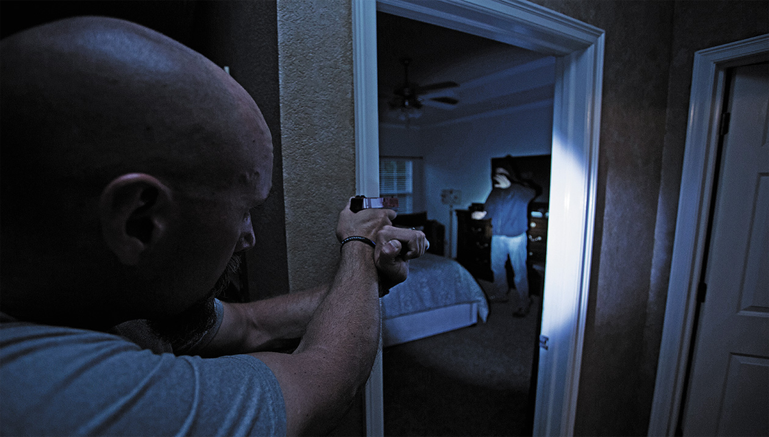 A homeowner using a flashlight to spot an intruder and issue verbal commands.
